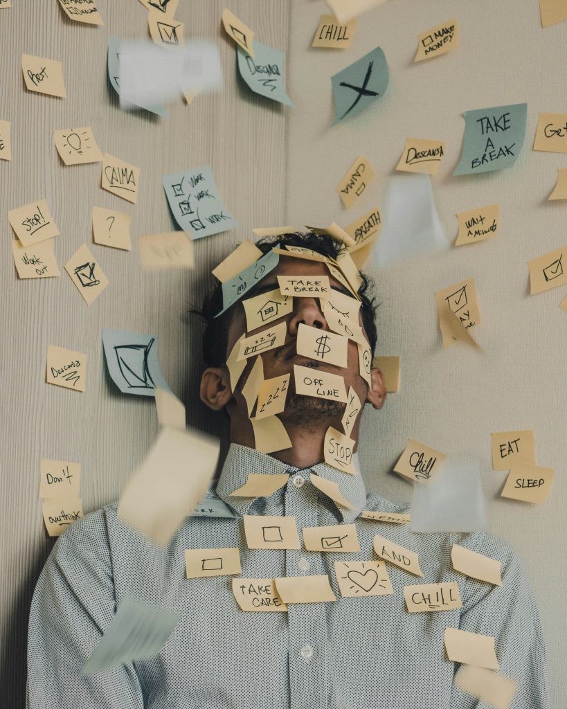 Dauerstress erkennen, bevor dein Körper stoppt Mann mit geschlossenen Augen, umgeben von vielen Post-its mit Aufgaben und To-dos – Symbolbild für Dauerstress und mentale Überlastung