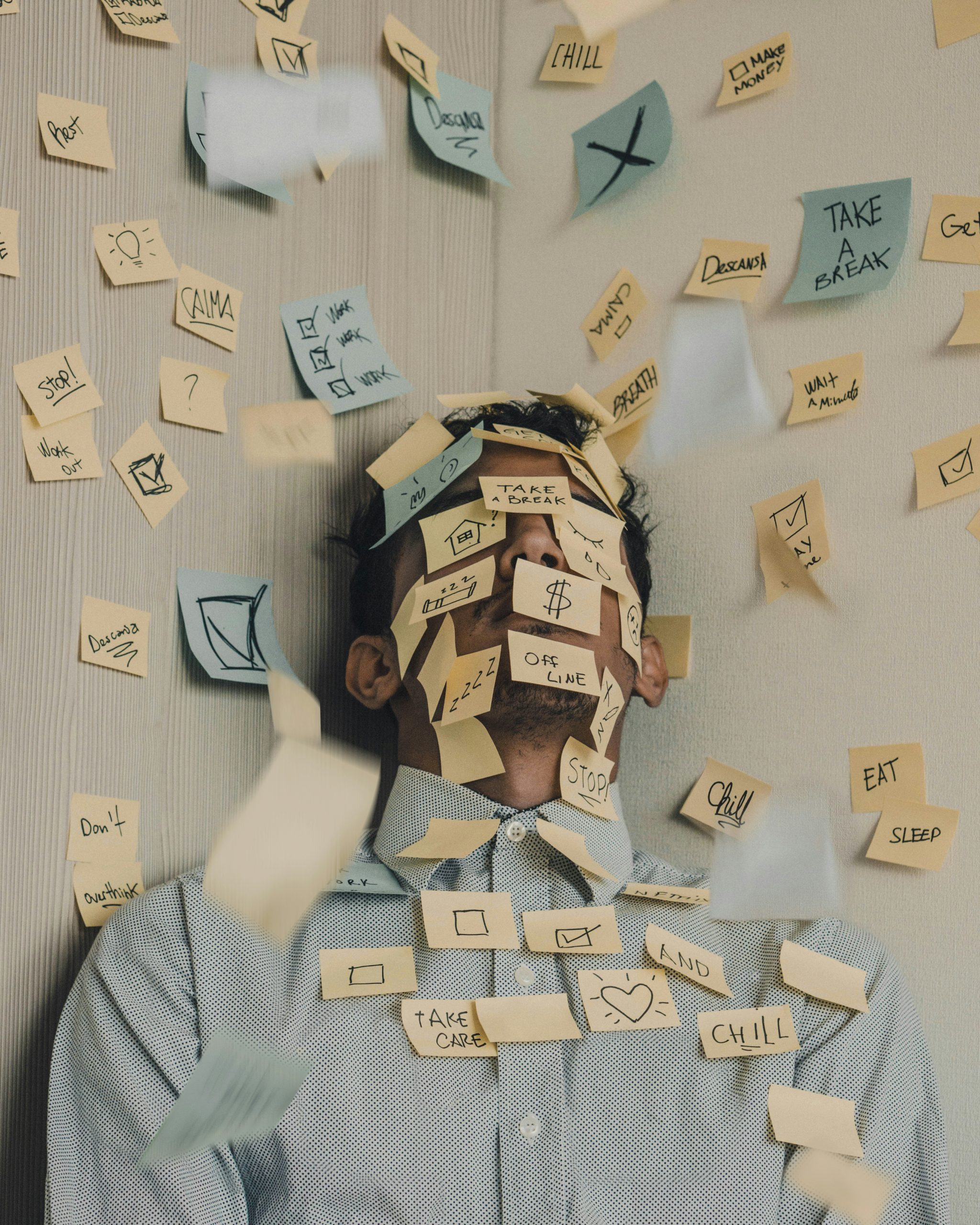 Mann mit geschlossenen Augen, umgeben von vielen Post-its mit Aufgaben und To-dos – Symbolbild für Dauerstress und mentale Überlastung