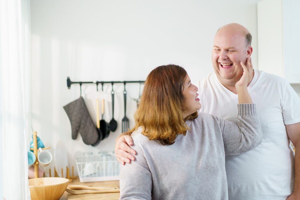 Wie du als Paar Eltern bleibst, ohne euch zu verlieren Paar steht lachend in der Küche und zeigt liebevolle Nähe im gemeinsamen Alltag