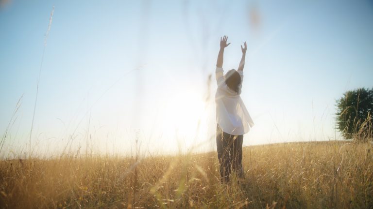 woman standing with her arms raised amidst vast wheat field
